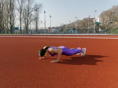 Woman doing a workout outdoors, she is doing push ups at the athletic stadium.