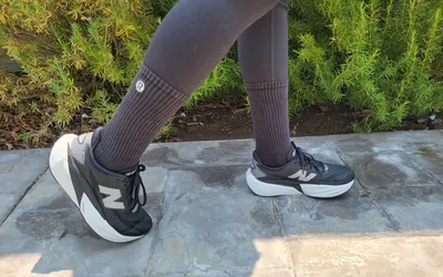 Closeup of a person walking wearing leggings, New Balance sneakers, and lululemon socks on a tiled sidewalk.