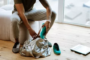 Putting sneakers. Close up of dark-skinned sportsman with tattoo putting sneakers into bag before going to gym