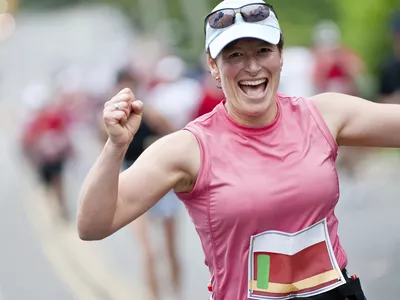 Woman smiles broadly and pumps her fists in celebration having completed first 30 of 42 kilometers in her first marathon race.