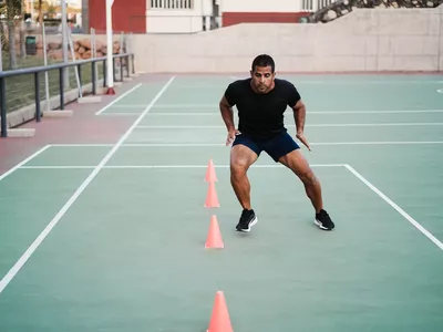 Hispanic man doing speed and agility cone drills workout session outdoors - Focus on man face
