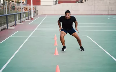 Hispanic man doing speed and agility cone drills workout session outdoors - Focus on man face