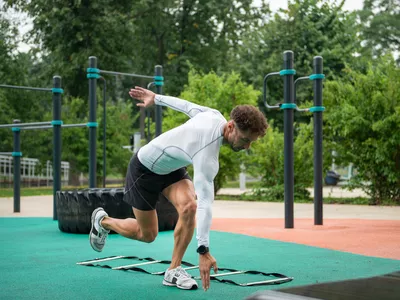 Male athlete standing on one leg exercising with speed ladder on the sports ground