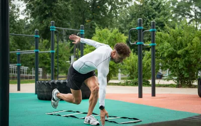 Male athlete standing on one leg exercising with speed ladder on the sports ground