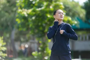 Portrait of Asian woman wearing earphones listening to music was sick with irritate itching her skin at park. Woman exercise at park itching her skin.