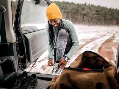 Woman pulls her training gear out of the trunk to exercise in the open on the snow