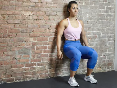 Woman doing a wall sit against a brick wall in gym