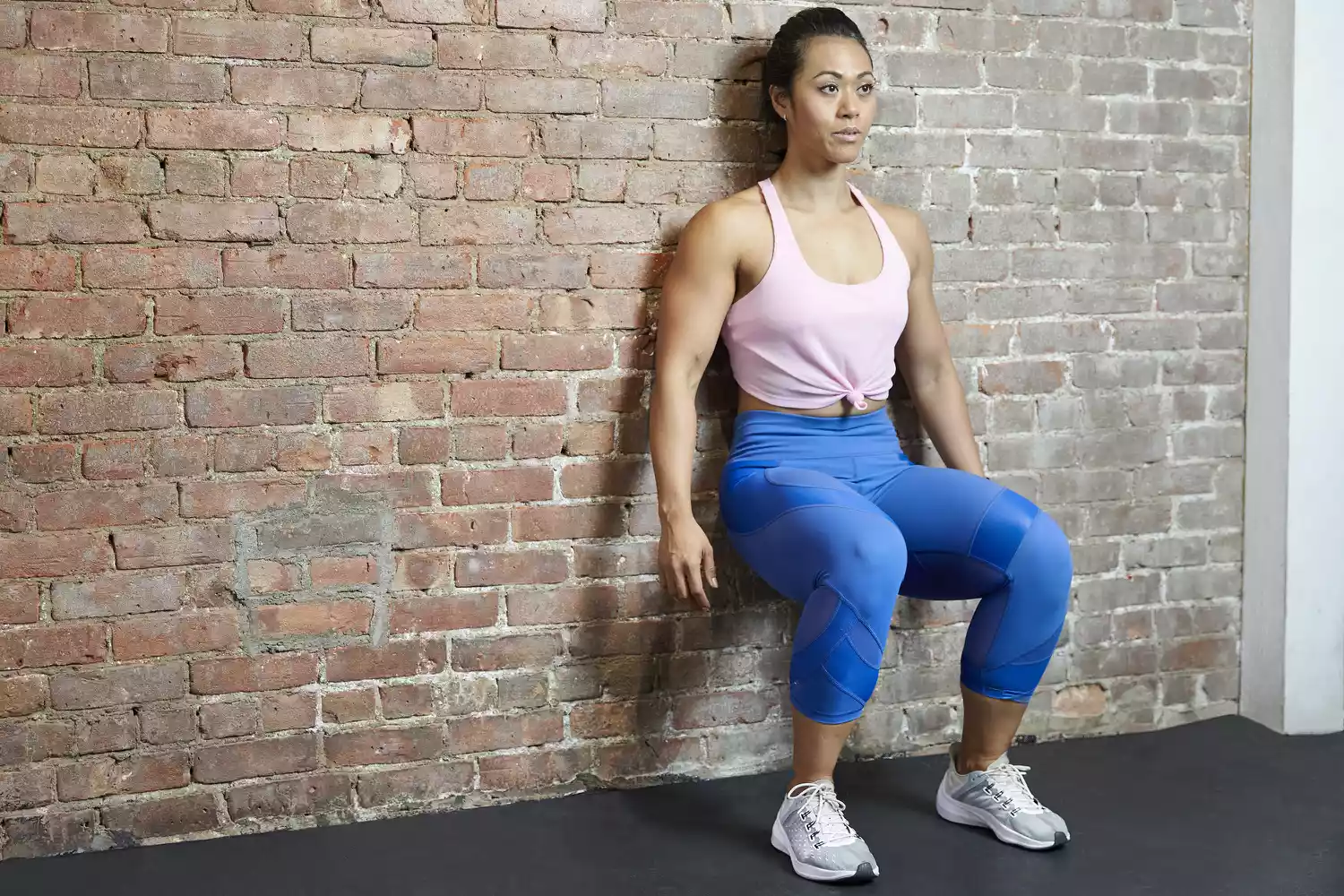 Woman doing a wall sit against a brick wall in gym