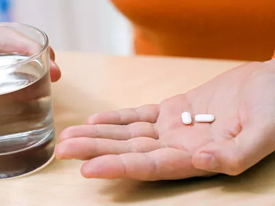Person holding two ibuprofen pills and a glass of water