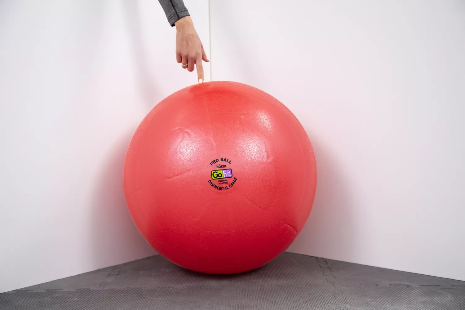 Person touching fingertip to GoFit Pro Grade Stability Ball in corner of walls
