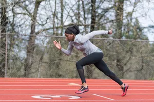 An African American female track athlete trains at a stadium. She is running sprints on the field. The shot is of her in profile as she runs from right to left.