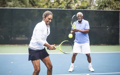 A Senior Black Couple Playing Doubles Tennis on a cloudy morning