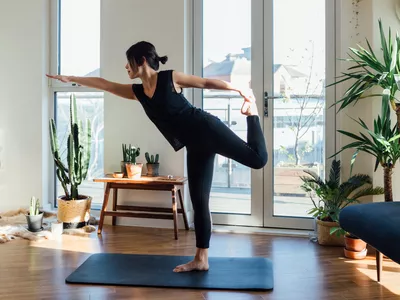 Woman performing single leg yoga pose in living room on yoga mat