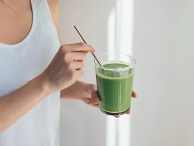 Woman in tank top holding green juice with a straw