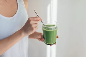 Woman in tank top holding green juice with a straw