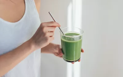 Woman in tank top holding green juice with a straw
