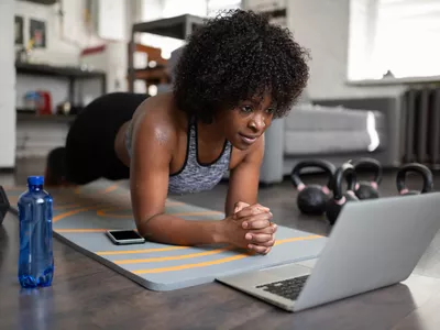 woman working out at home with laptop nearby