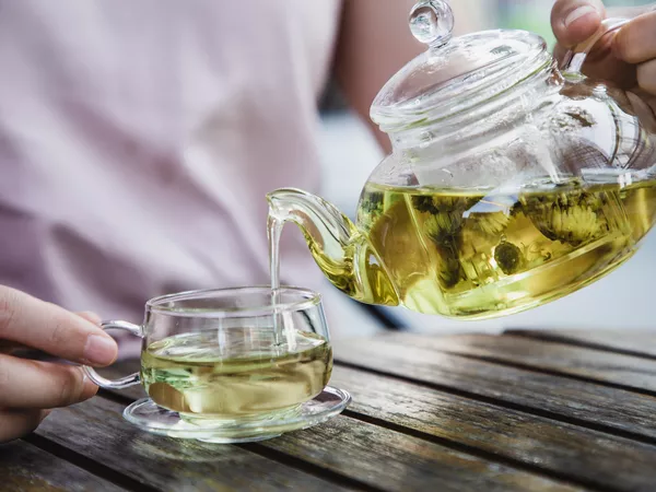 Hands pouring a glass kettle of green tea