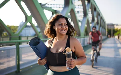 Woman walking on bridge with yoga mat and water bottle
