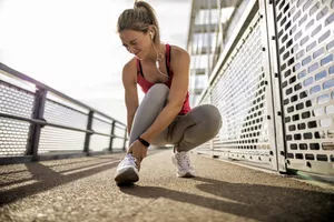 Woman cringing with pain while holding her foot while running outdoors.