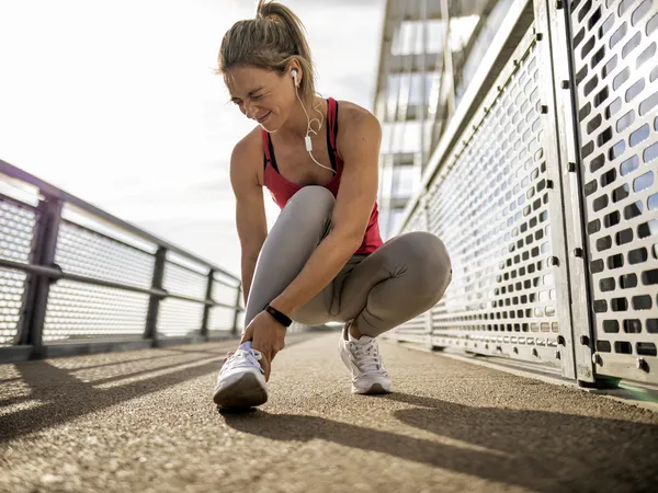 Woman cringing with pain while holding her foot while running outdoors.