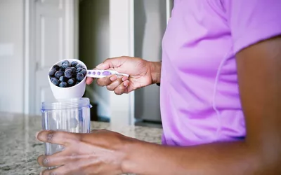 Person pouring blueberries into a blender