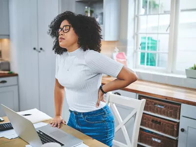 Young Black woman with back pain standing at desk