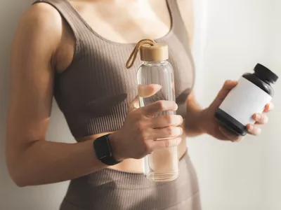 Cropped photo of female's hands holding bottle of water and bottle of vitamins or protein. Healthy lifestyle and sport concept