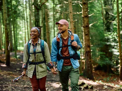 Couple rucking in the woods with rucksacks holding hands.