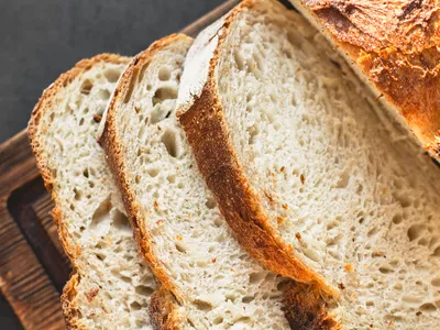 Top view of appetizing homemade sliced gluten free bread with crispy crust on wooden board on dark table. Long banner for design, web site