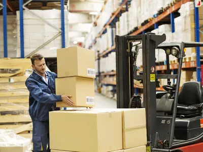 Male worker loading cardboard boxes on forklift at distribution warehouse