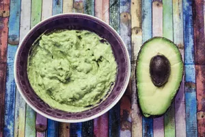 Bowl of guacamole and sliced avocado on colorful surface