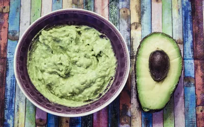 Bowl of guacamole and sliced avocado on colorful surface