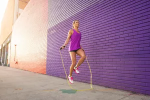 woman jumping rope outdoor with purple brick background