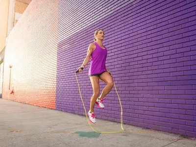 woman jumping rope outdoor with purple brick background