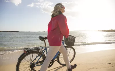 Woman pushes bike along sandy beach