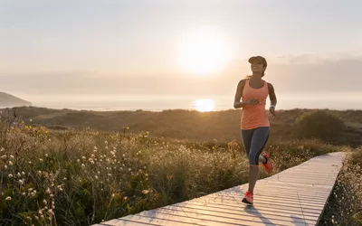 Spain, Aviles, young athlete woman running along a coastal path at sunset