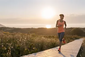 Spain, Aviles, young athlete woman running along a coastal path at sunset