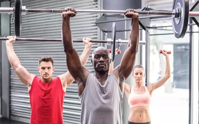 Three athletes perform a barbell overhead shoulder press.