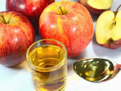 Glass of apple juice, spoonful of apple cider vinegar, and several apples