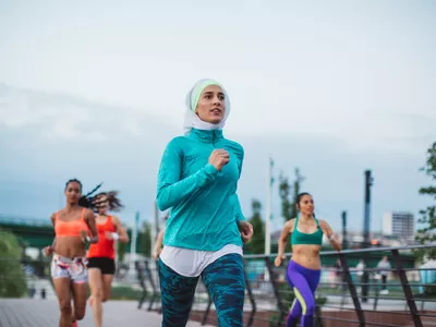 Multi ethnic group of young women exercise outdoor, next to the river. They are wearing sport clothing, running, stretching, celebrate, and support each other. 