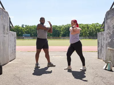 Two walkers stretching near track in fitness apparel with water bottles and towel 