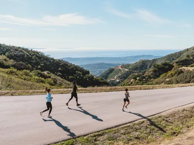 three runners jogging downhill on mountain road