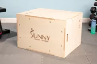 Sunny Health & Fitness High-Capacity Wooden Plyo Box on floor near fitness equipment