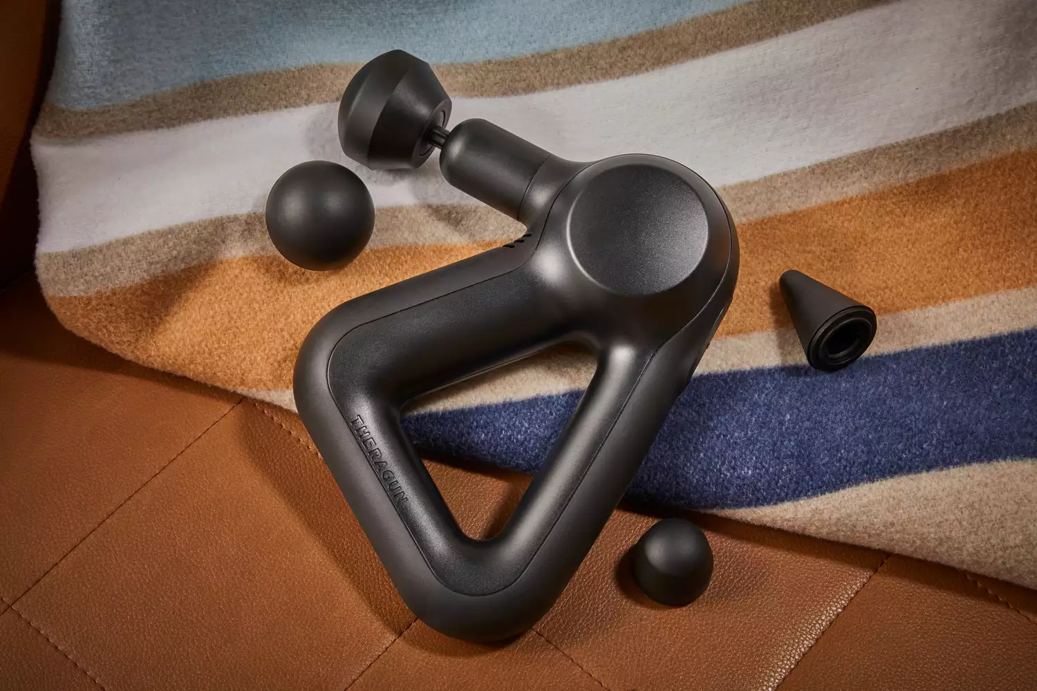 Therabody Theragun Prime Massage Gun displayed with accessories on a blanket