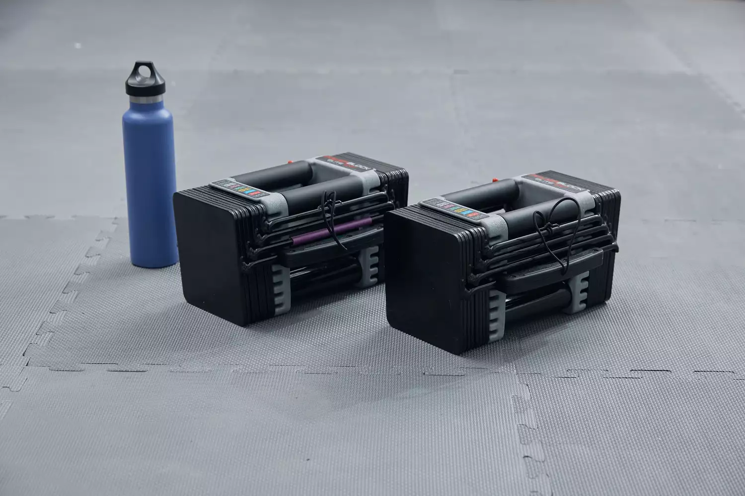 PowerBlock Elite Adjustable Dumbbells with water bottle on gray mat