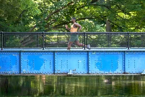 man running across a blue bridge with park in background