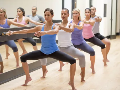 a line of exercisers doing a barre workout plié squat