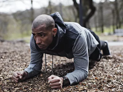 Determined male athlete performing plank position in forest
