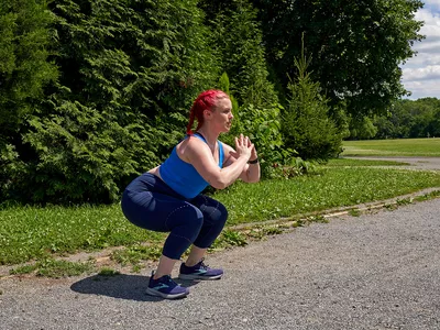 woman doing squats on a paved path in a park